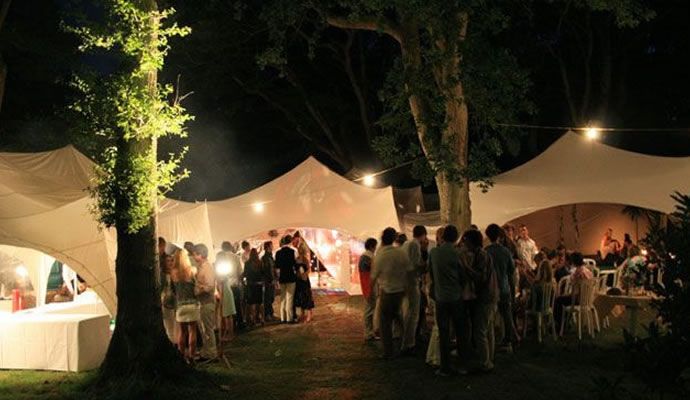 Outdoor party at night with festoon lighting between marquees and trees