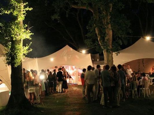Outdoor party at night with festoon lighting between marquees and trees